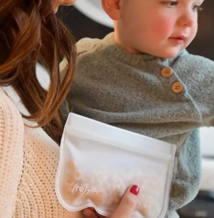 A toddler holding a rezip bag with snacks in it.